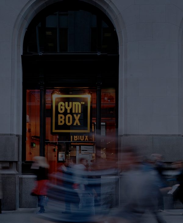 The front of Gymbox Bank showing people walking past very quickly depicting a busy London St. The Gymbox Logo can be seen in the window behind