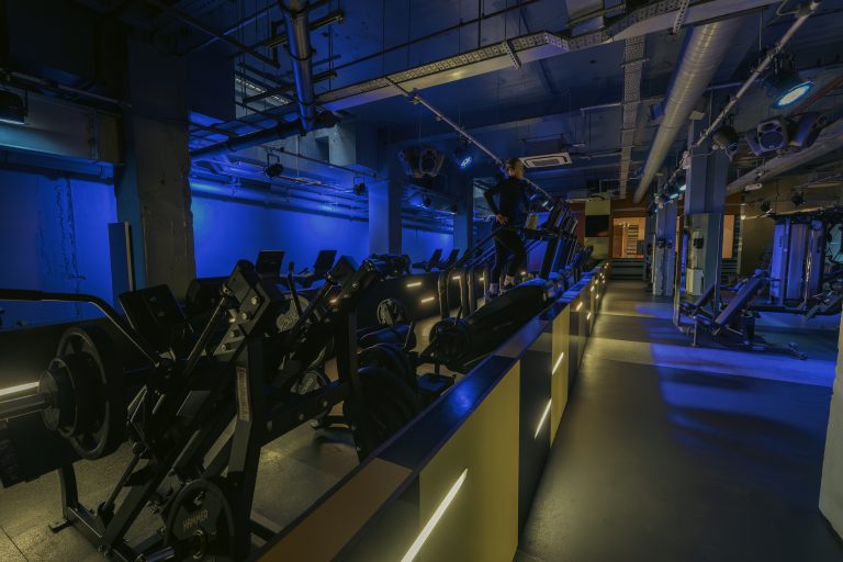 Gymbox Bank is the best Gym in Bank showing cardio area with treadmills and resistance machines, set under blue nightclub design lighting.
