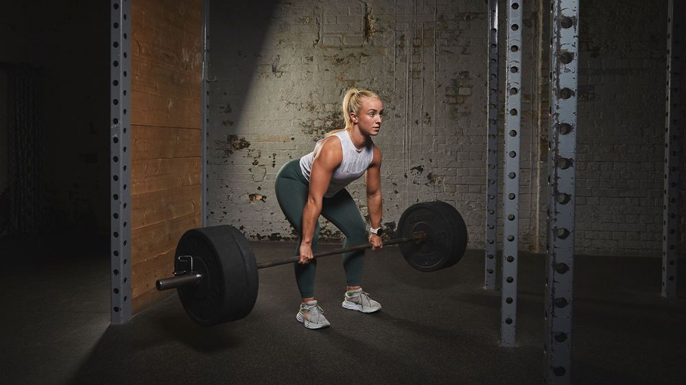 WOD Squad HVY - Woman in sportswear performs deadlift with a barbell