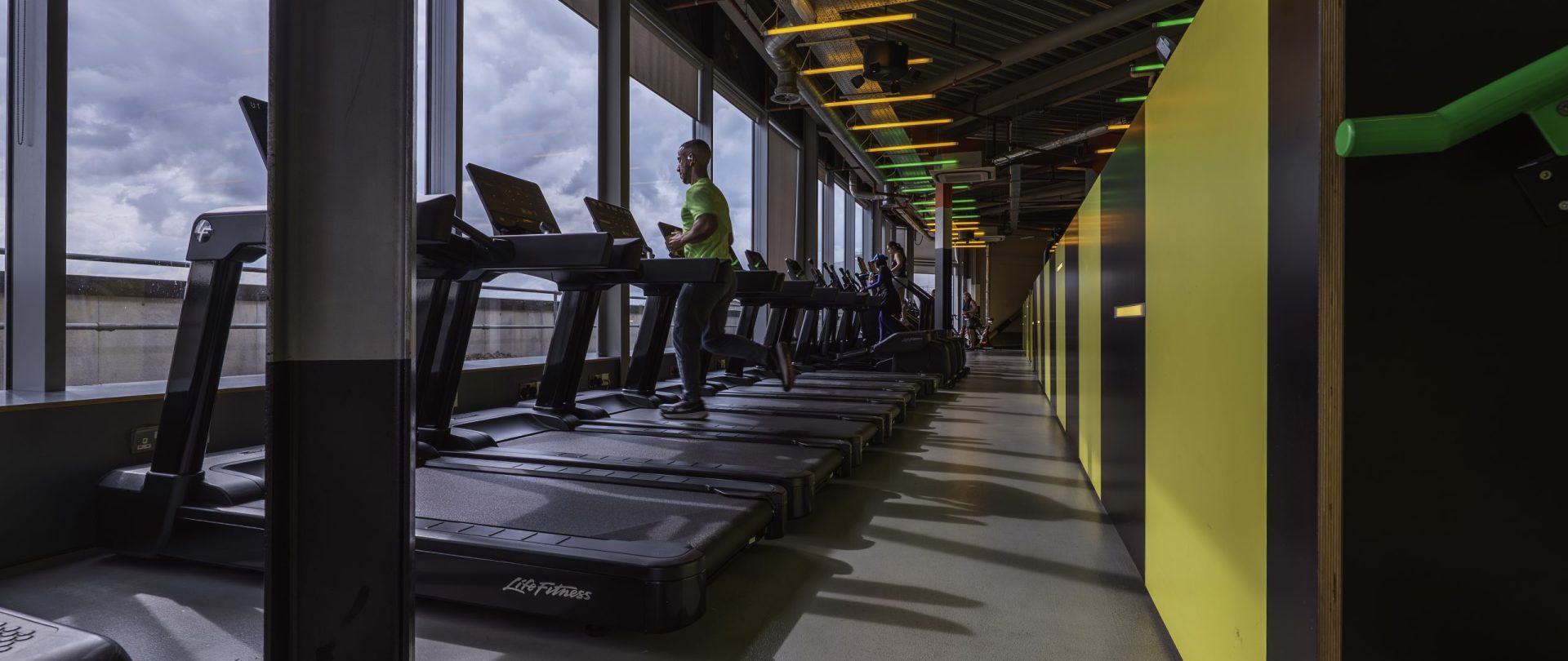 Gymbox Westfield London, showing the cardio area with treadmills, in front of a panoramic view of London and nightclub design lighting overhead