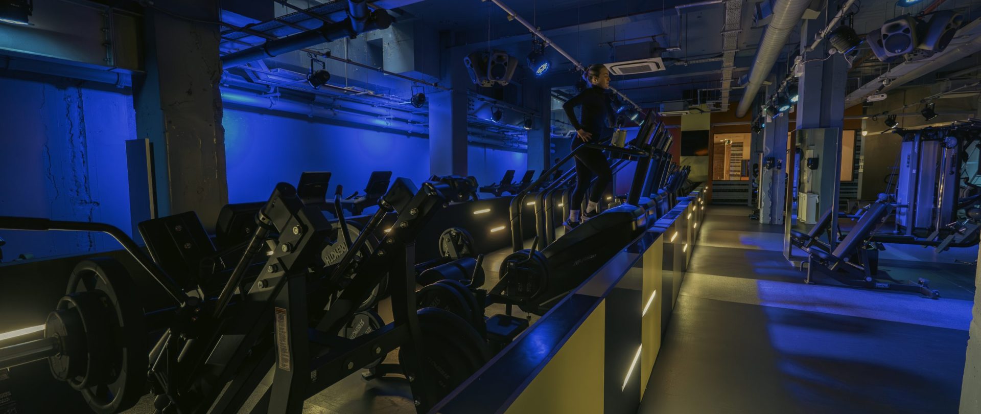 Gymbox Bank is the best Gym in Bank showing cardio area with treadmills and resistance machines, set under blue nightclub design lighting.